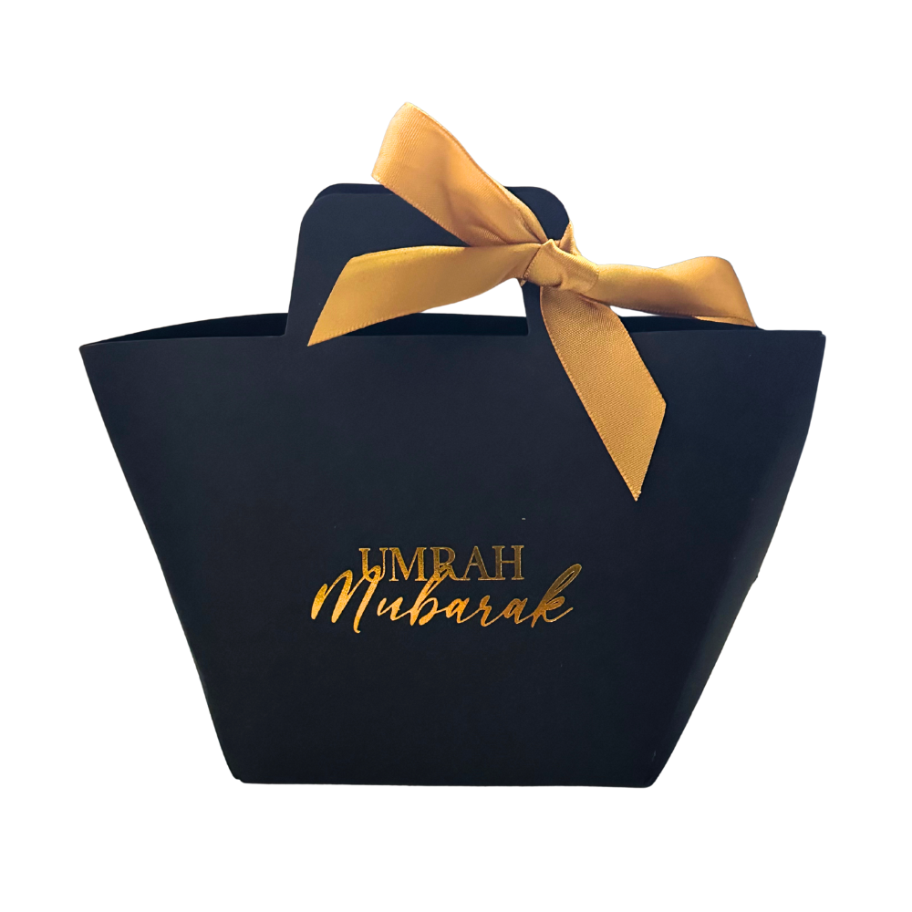 Black gift bag with gold 'Umrah Mubarak' text and a gold ribbon on a white background